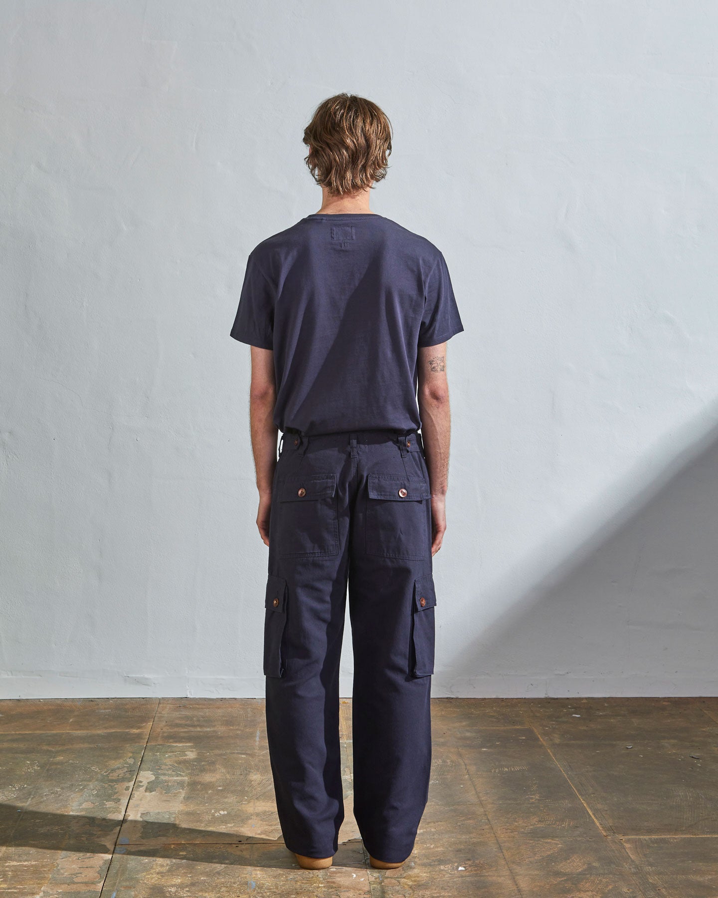 Full length back-view of model wearing midnight blue organic cotton #5014 trousers with view of rear and cargo pockets. Paired with matching t-shirt.