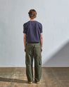Full length back-view of model wearing vine green organic cotton #5014 trousers with view of rear and cargo pockets. Paired with midnight blue t-shirt.