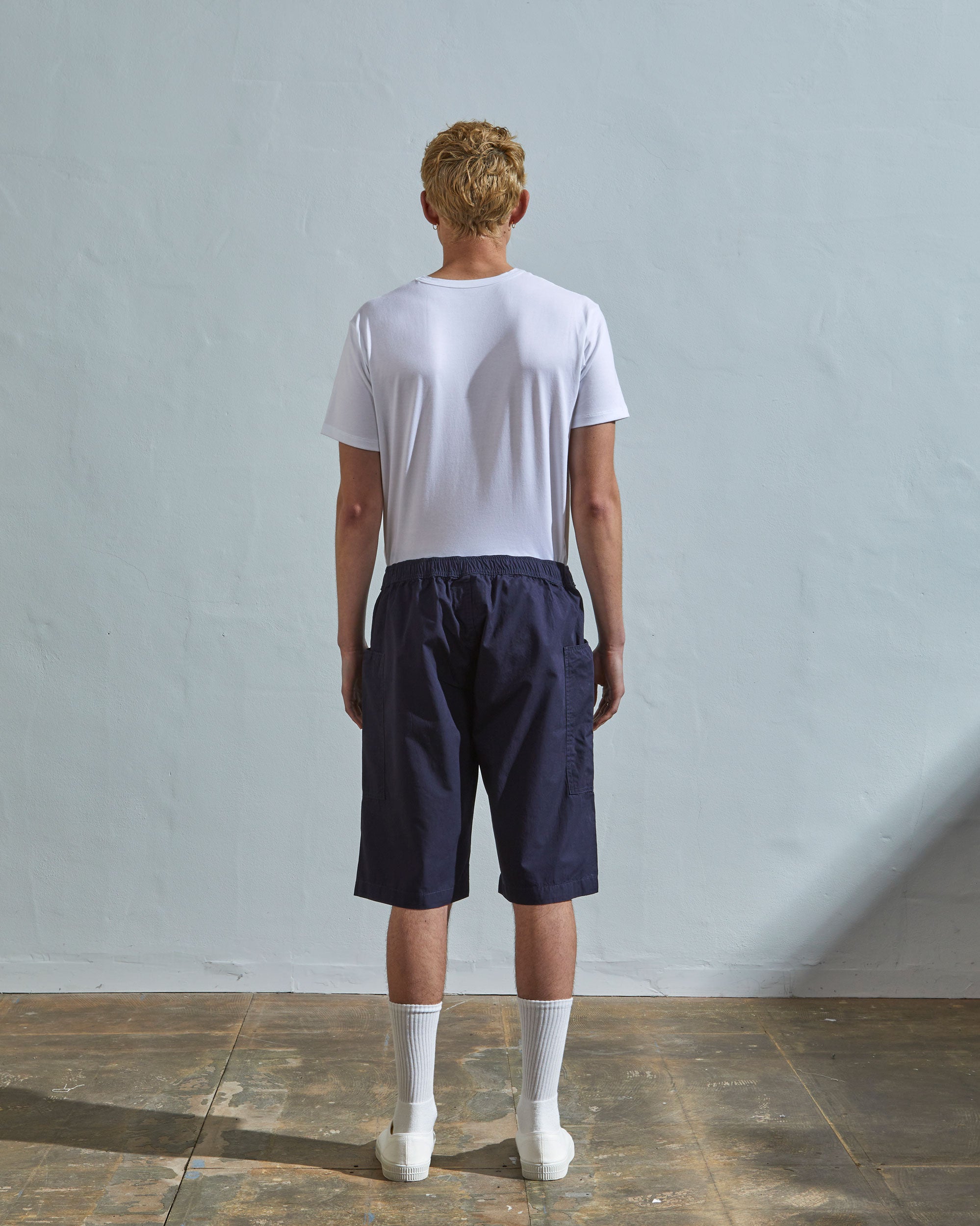Back view of model wearing midnight blue, loose leg light organic cotton shorts by Uskees. Large front pockets visible.
