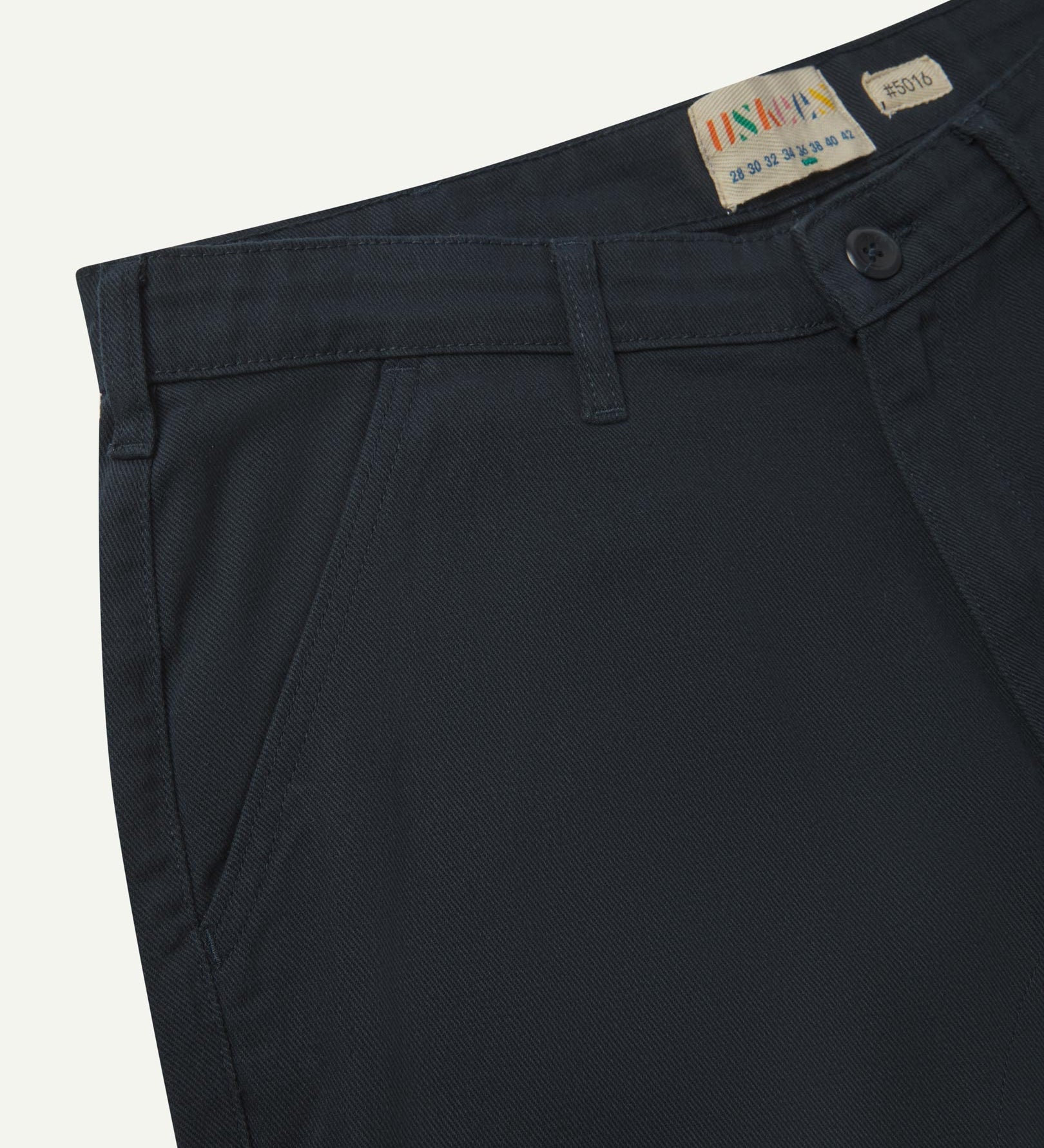 Close-up front view of the left-front pocket, belt loops and Corozo button of blueberry heavyweight drill pants.