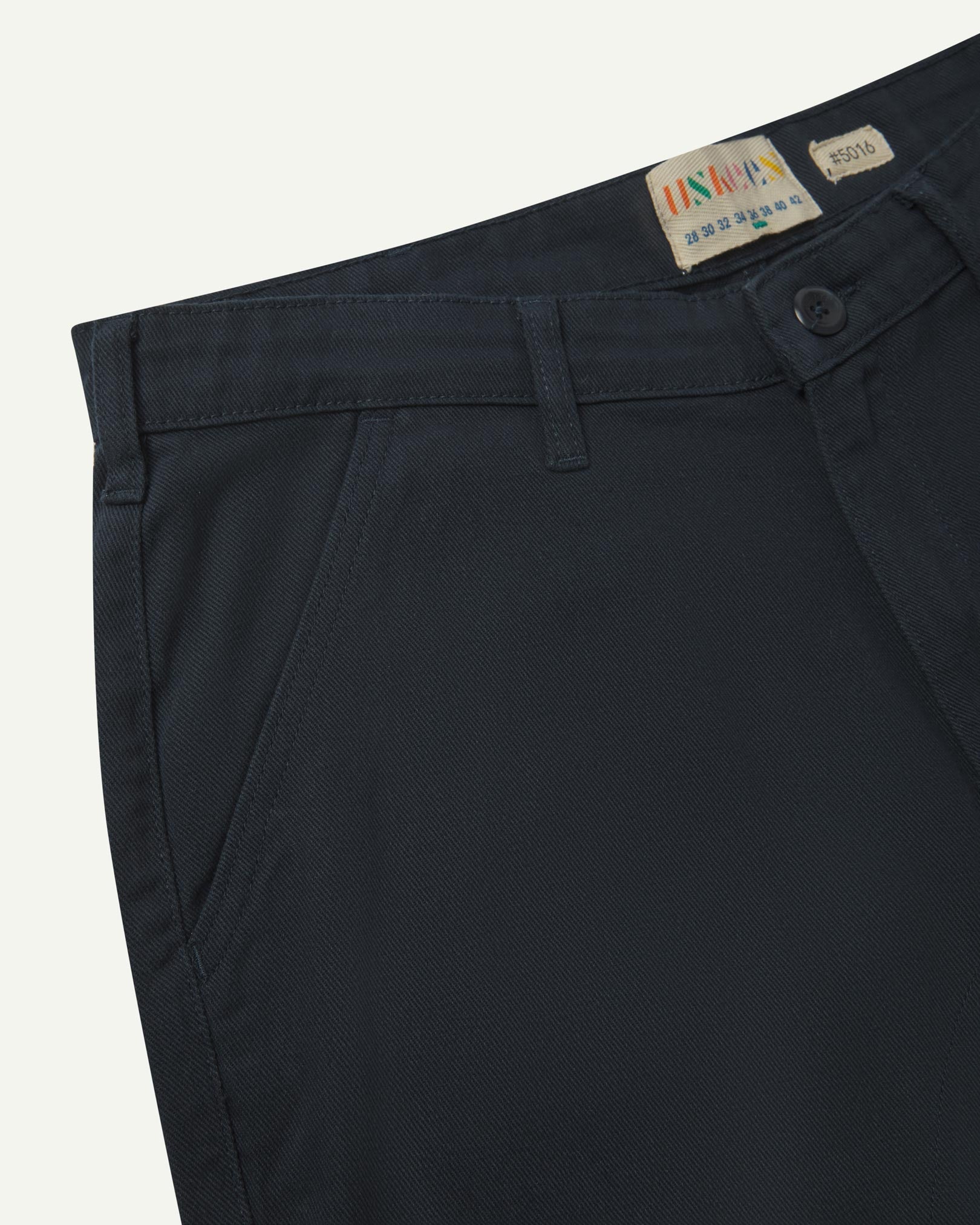 Close-up front view of the left-front pocket, belt loops and Corozo button of blueberry heavyweight drill pants.