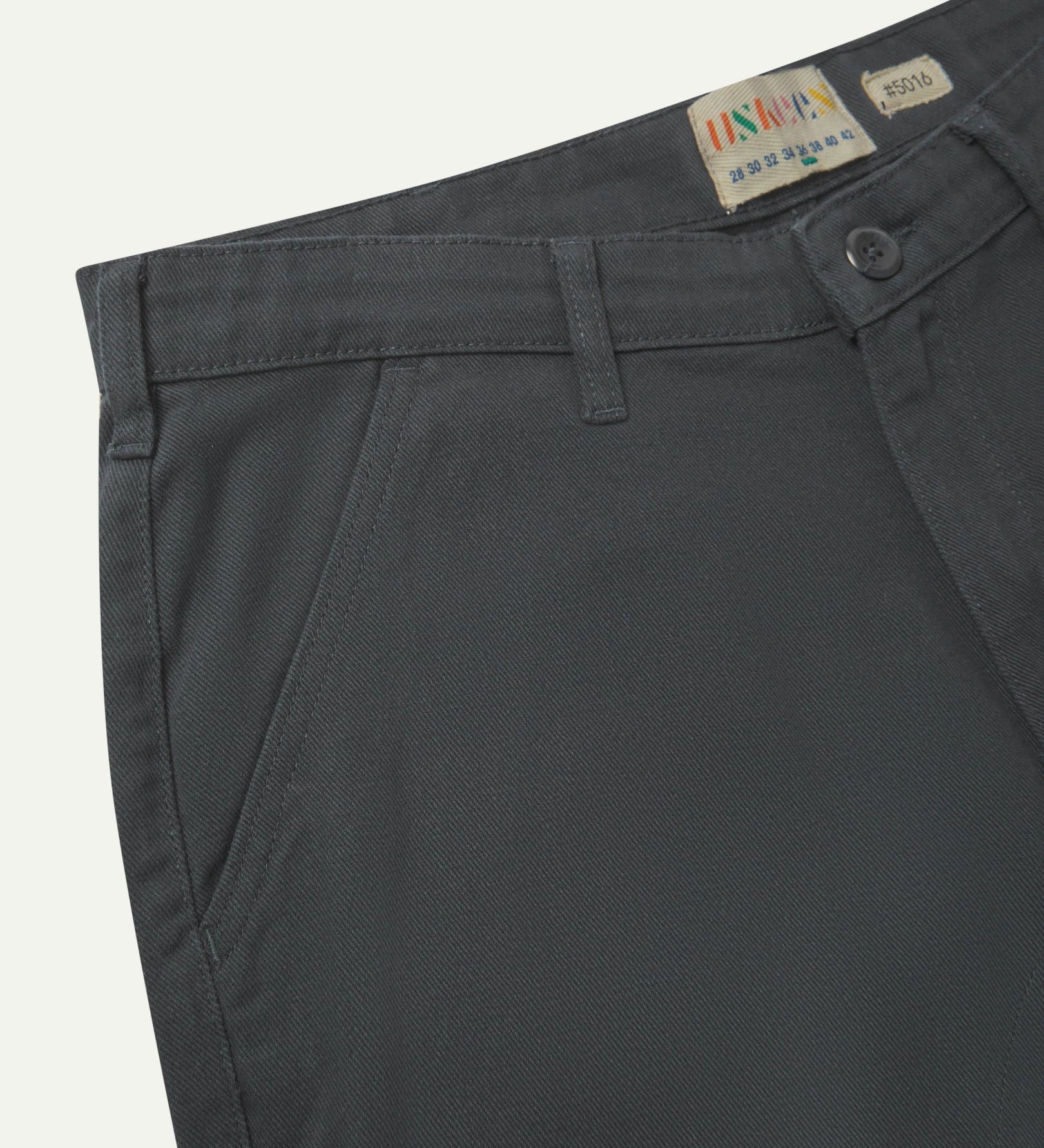 Close-up front view of the left-front pocket, belt loops and Corozo button of charcoal grey heavyweight drill pants.