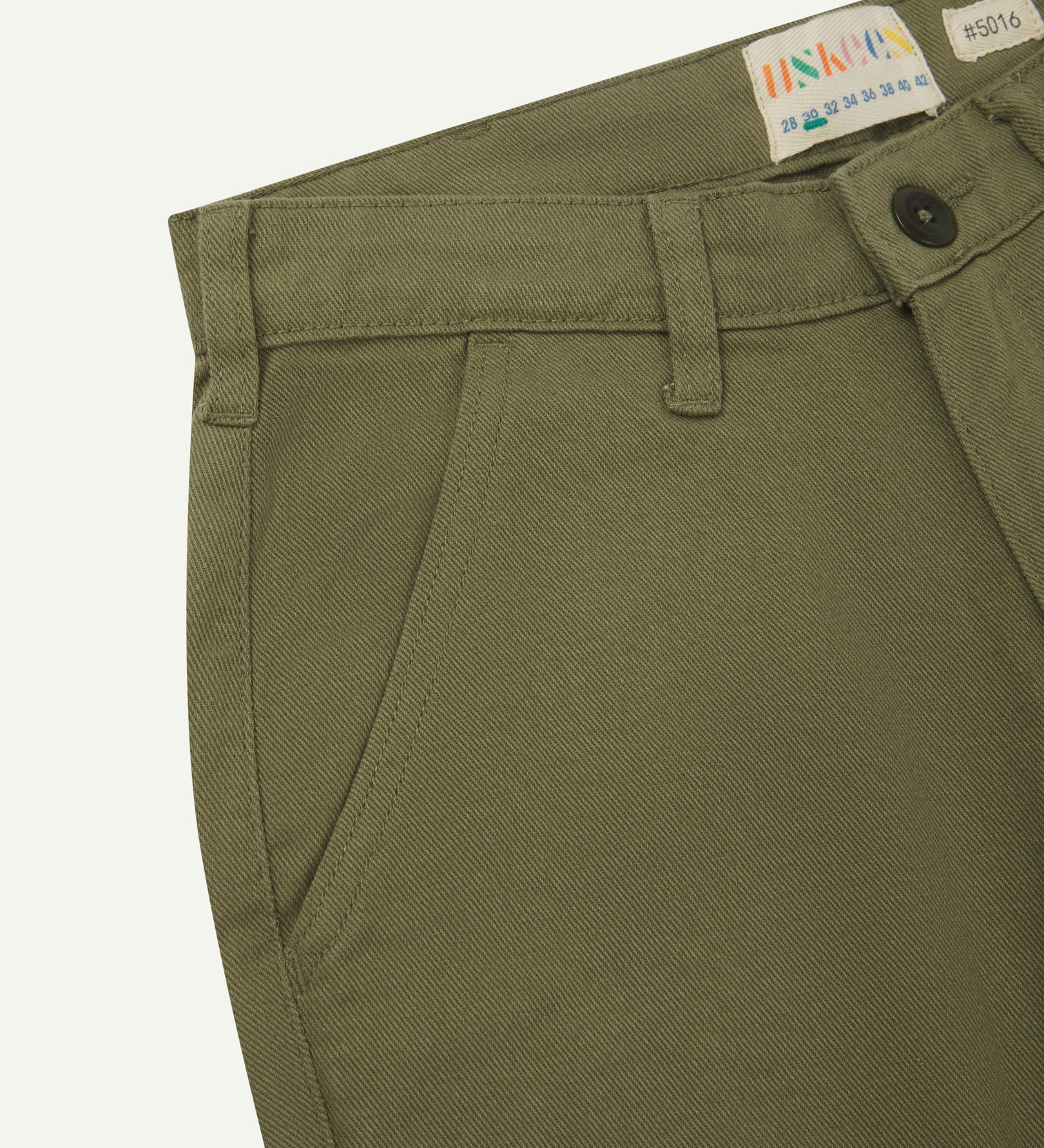 Close-up front view of the left-front pocket, belt loops and Corozo button of moss green heavyweight drill pants.