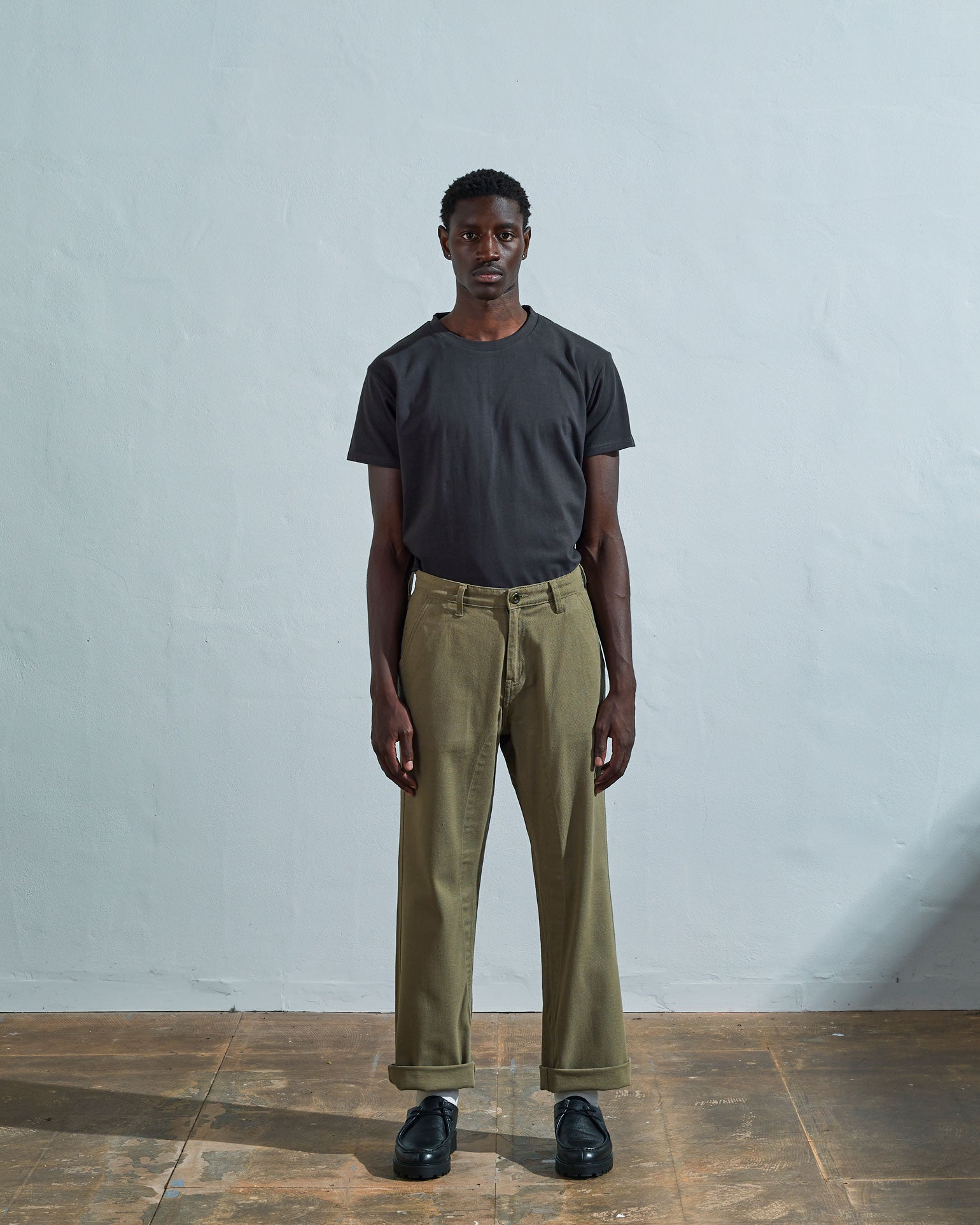 Full-length front view of model wearing #5016 drill commuter pants in moss with turn-ups, paired with Uskees faded black tee.