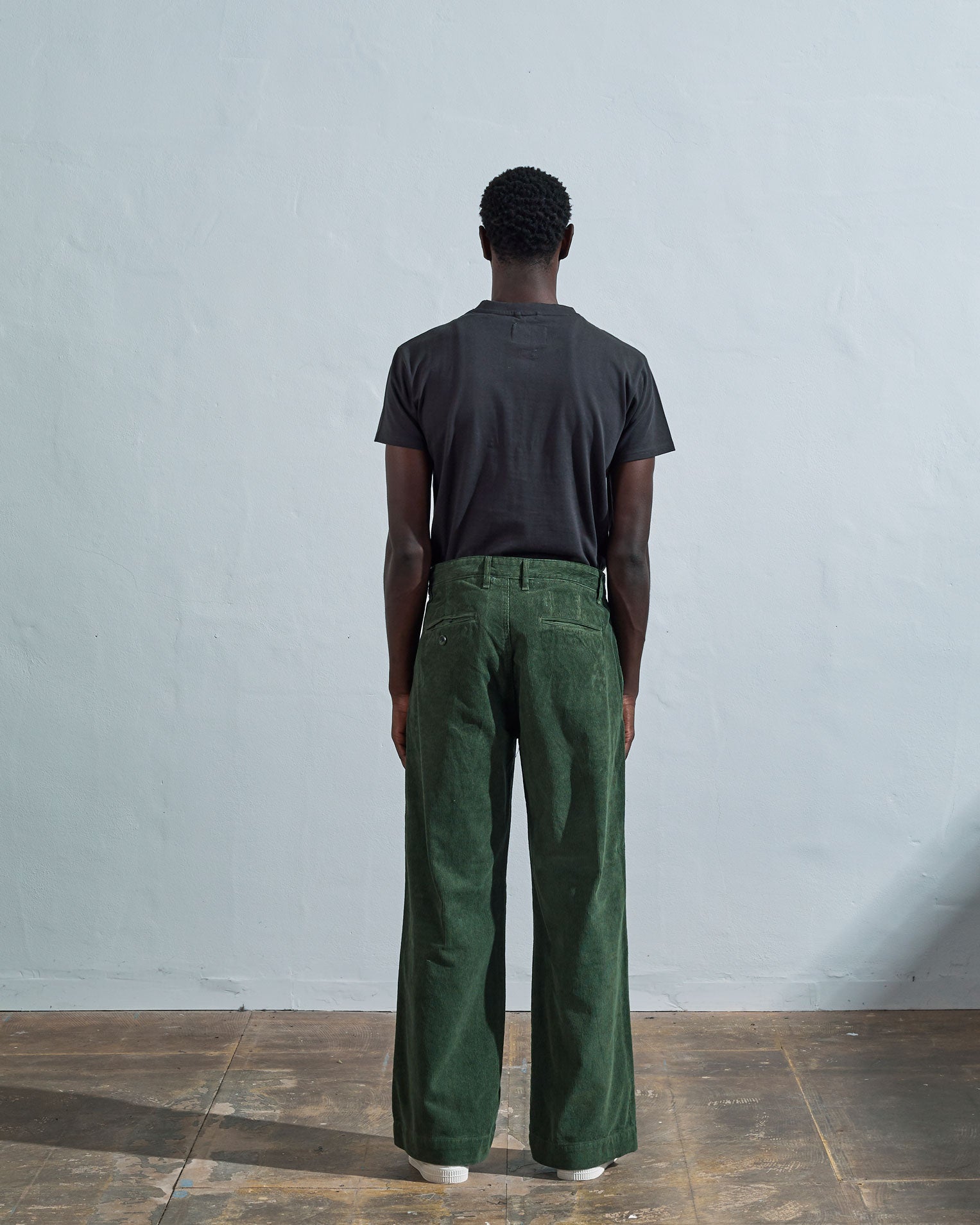 Full length back-view of model wearing coriander-green corduroy #5018 trousers with view of rear pockets and belt loops and demonstrating vintage wide leg fitting.