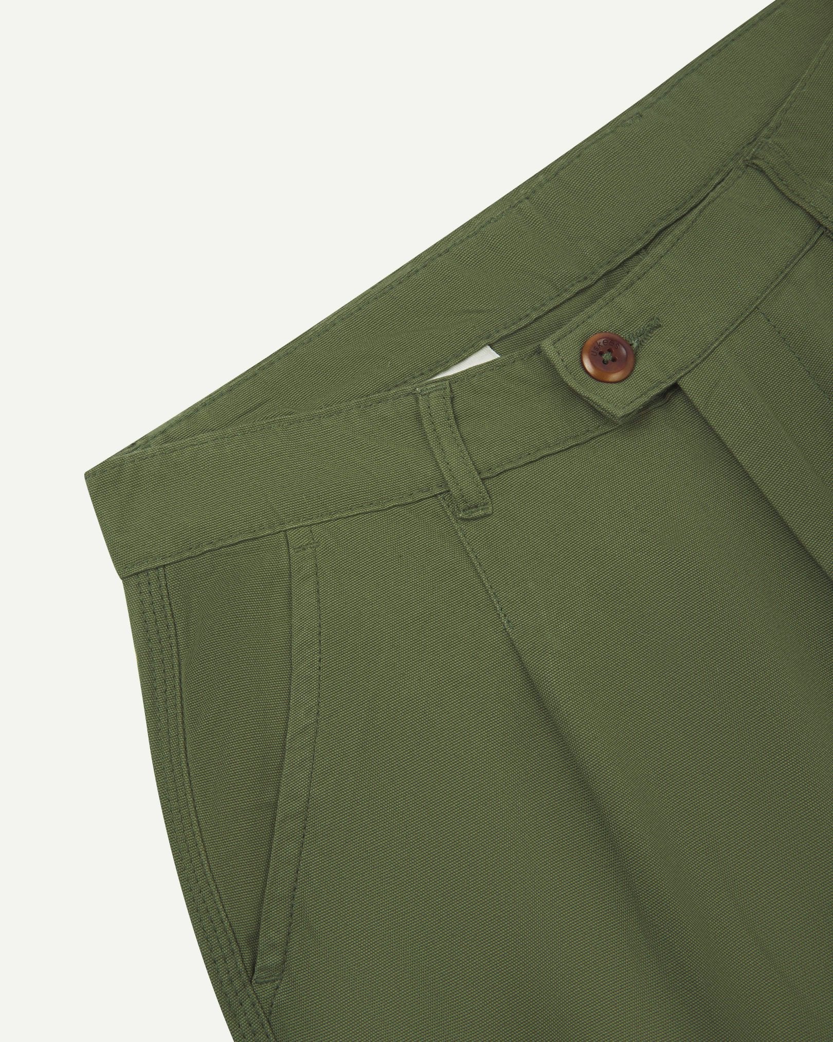 Front close-up shot of 5018 Uskees men's organic mid-weight cotton boat trousers in coriander-green showing corozo button fastening at waistband, belt loops and front pocket.