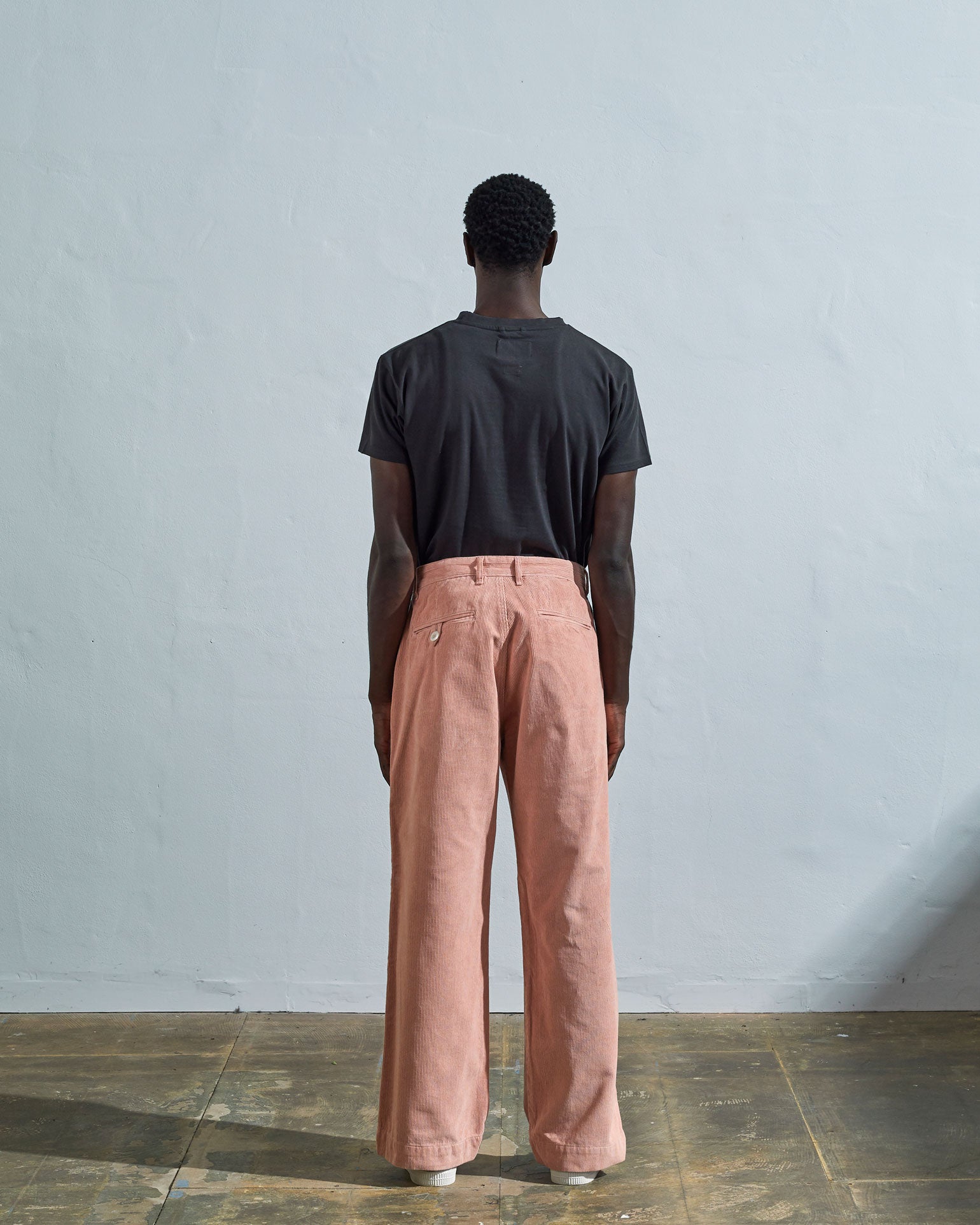Full length back-view of model wearing dusty-pink corduroy 5018 trousers with view of rear pockets and belt loops and demonstrating vintage wide leg fitting.