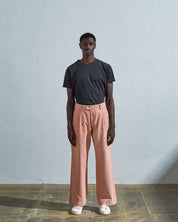 Full length front-view of model wearing dusty pink corduroy 5018 trousers with view of corozo button fastening. Paired with Uskees faded black t-shirt.