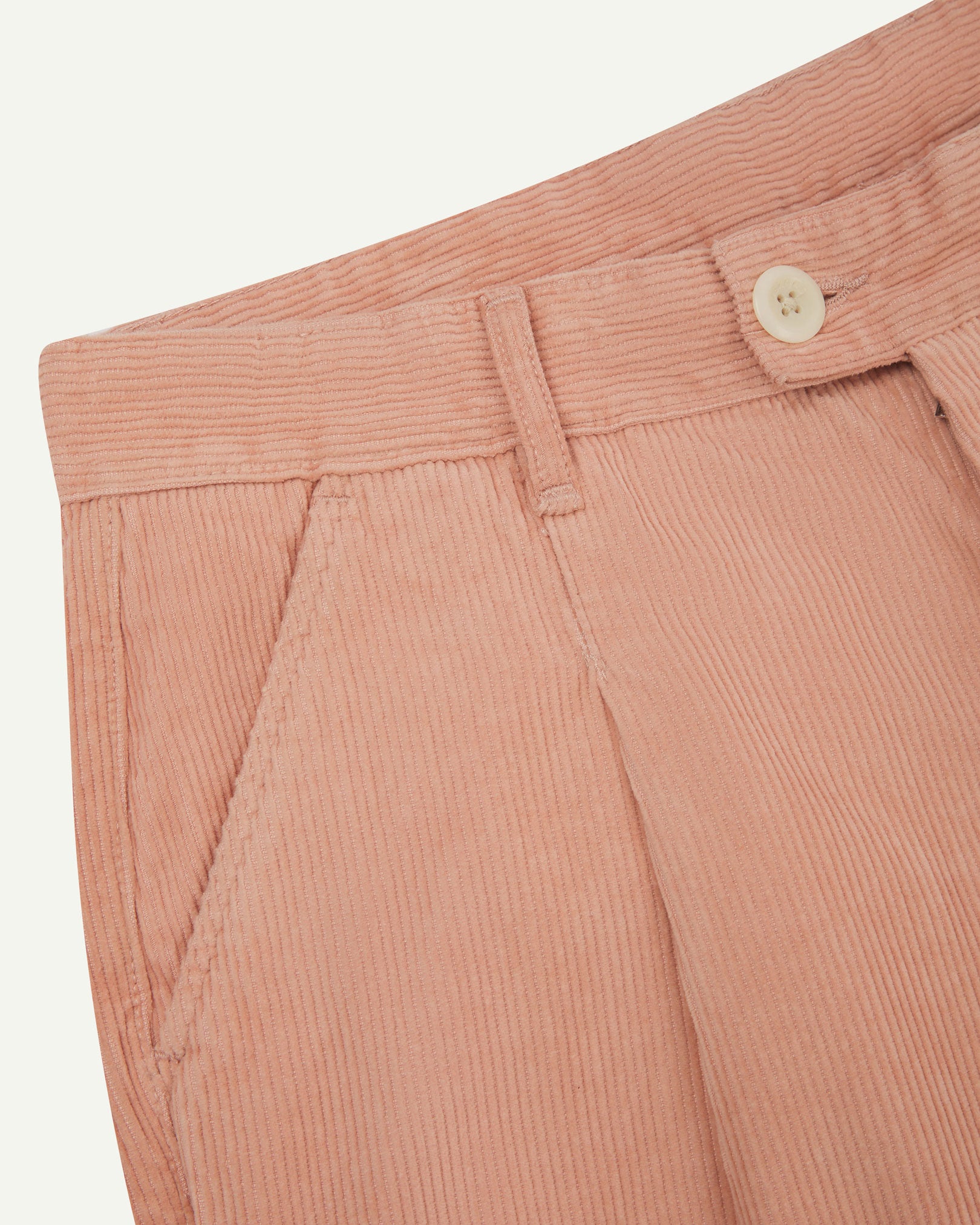 Close up of waist area of Uskees cord boat pants in dusty pink. Clear view of front pocket, belt loops and Corozo button fastening.