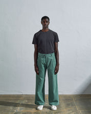 Full length front-view of model wearing eucalyptus corduroy #5018 trousers with view of corozo button fastening. Paired with Uskees faded black t-shirt.