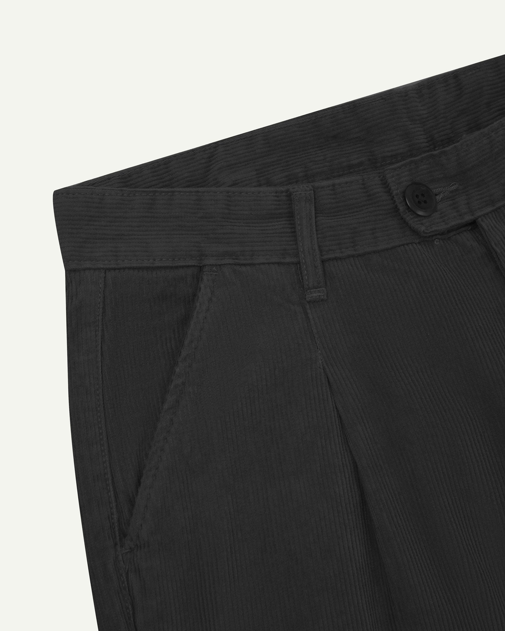 Close up of waist area of Uskees cord boat pants in faded black. Clear view of front pocket, belt loops and Corozo button fastening.