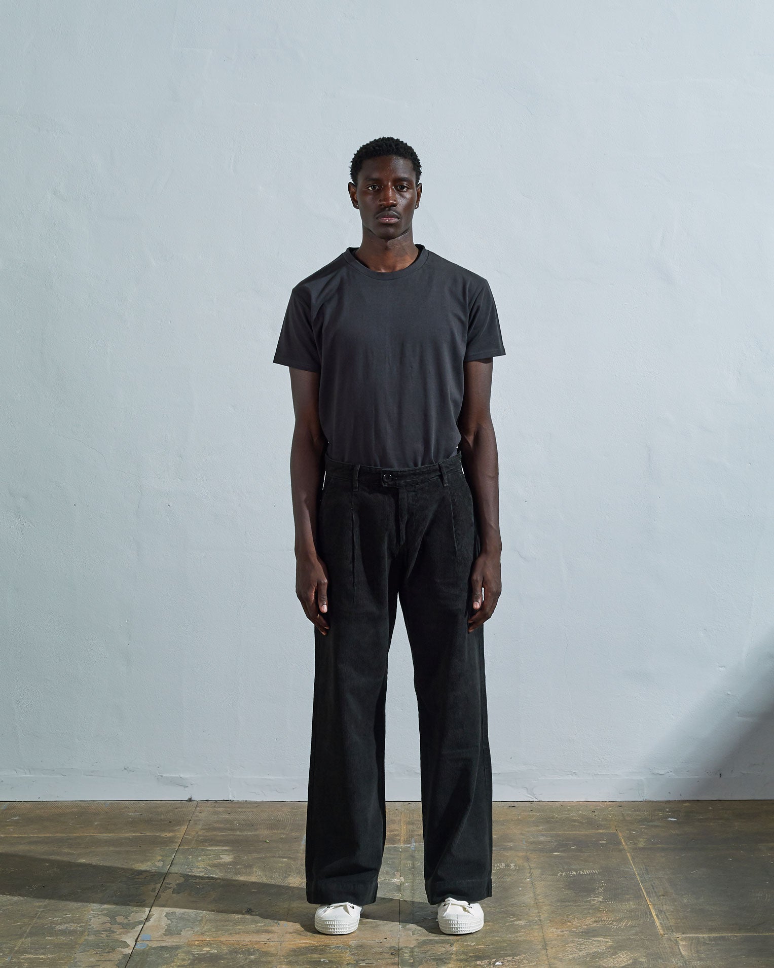 Full-length front view of model wearing Uskees #5018, faded black corduroy boat pants paired with faded black t-shirt.