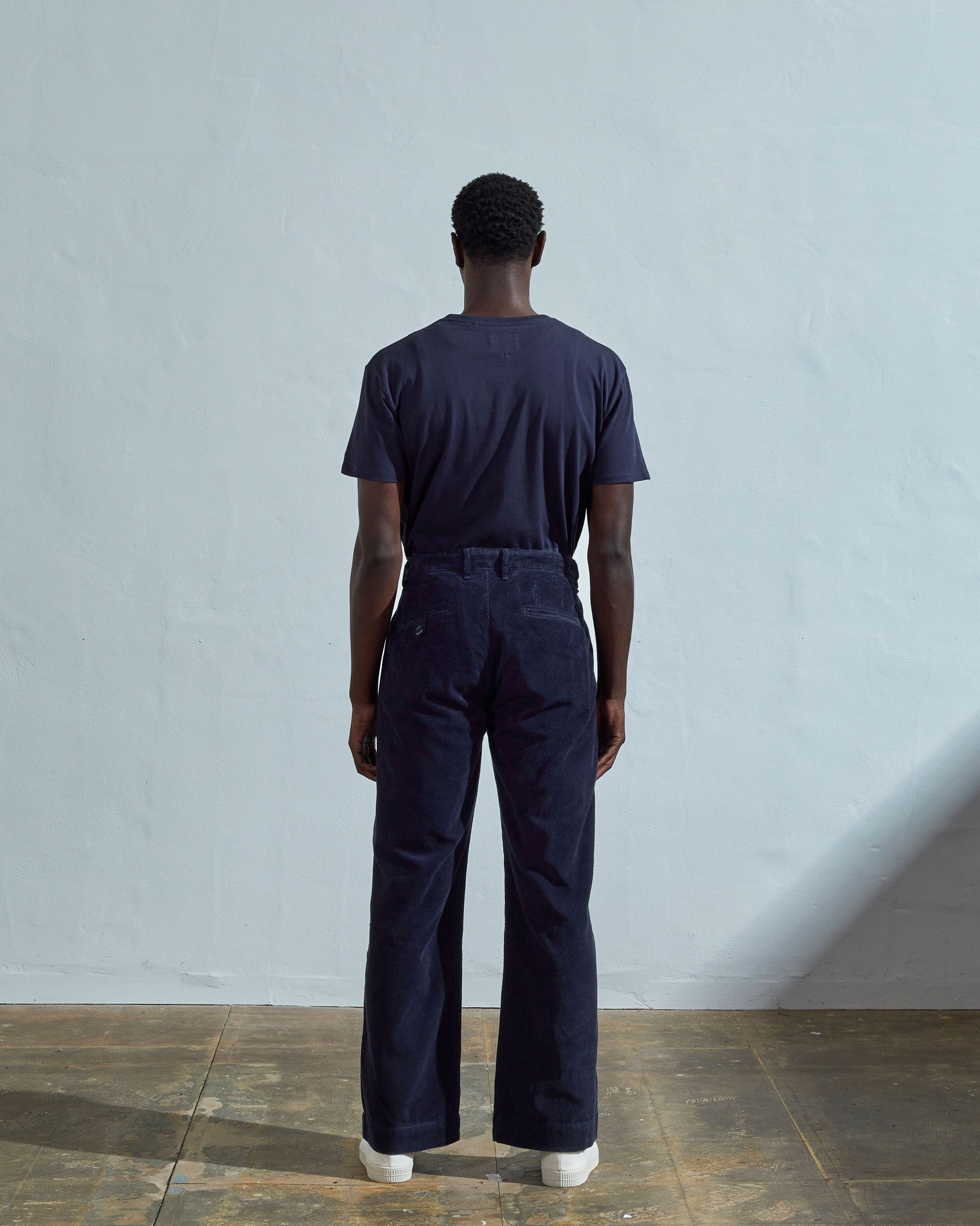 Full length back-view of model wearing midnight blue corduroy #5018 trousers with view of rear pockets and belt loops and demonstrating vintage wide leg fitting.