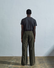 Full length front-view of model wearing vine green corduroy #5018 trousers with view of corozo button fastening. Paired with Uskees faded black t-shirt.