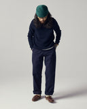 Male model wearing a navy sweater, Uskees dark blue painter pants, and green beanie on a plain background