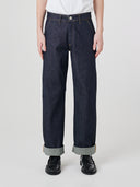Bottom-half front view of male model wearing Uskees raw orta denim workwear pants in dark indigo with turn-ups.
