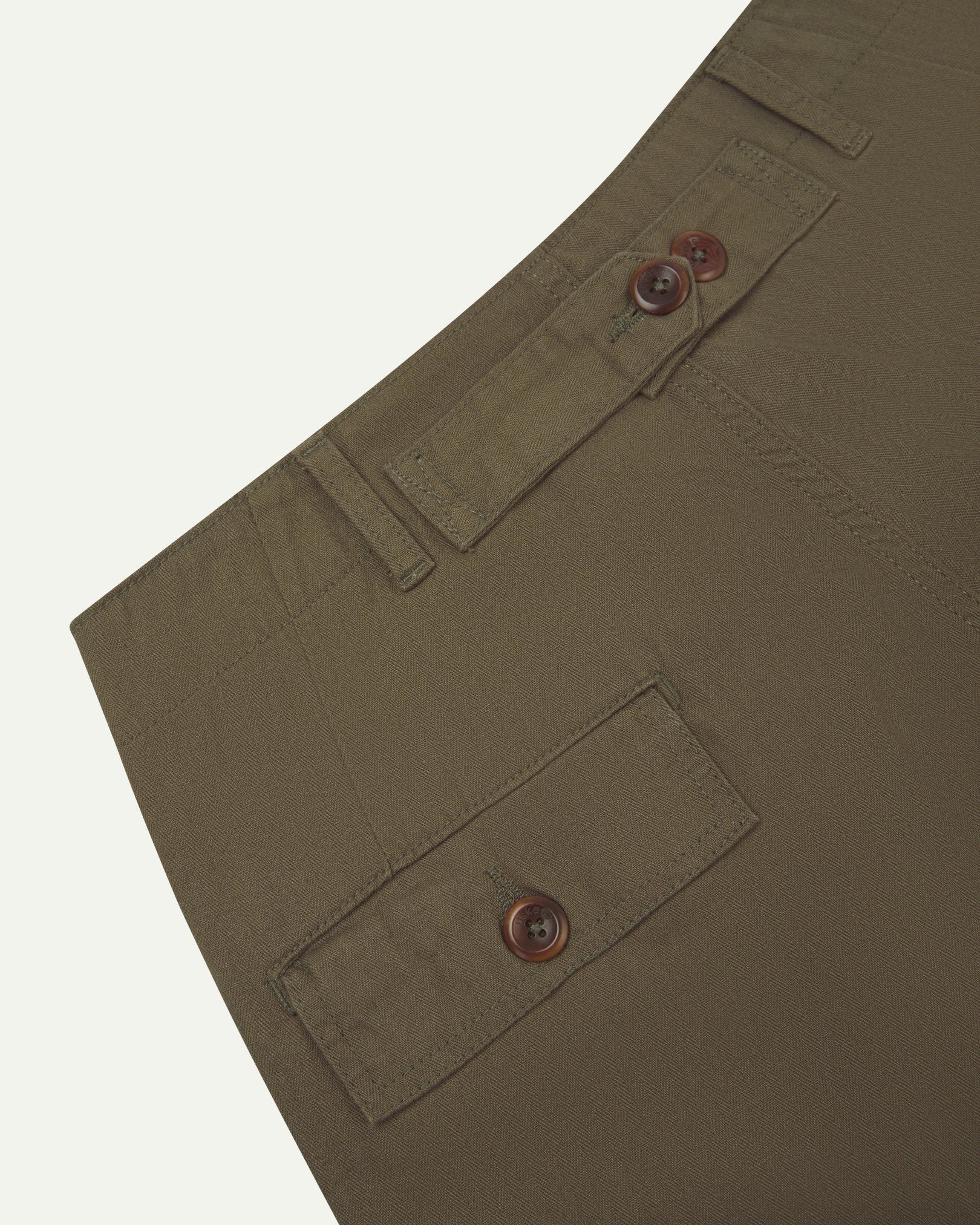 Close up, angled back view of Uskees 5022 barrel leg pants in dark taupe with focus on cinch strap, neat back pocket with flap, belt loops and durable herringbone fabric.