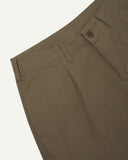 Close up, angled view of Uskees barrel leg pants waist area. Clear view of front pocket, belt loops, Corozo button fastening and organic cotton herringbone fabric.
