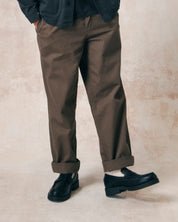 Closer front view of model wearing dark taupe 5022 barrel leg pants from Uskees. Showing button fly and herringbone textured fabric.