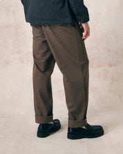 Closer side-back view of model wearing dark taupe 5022 barrel leg pants from Uskees. Showing baggy fit with taper at the hem, triple needle stitching and turn-ups.