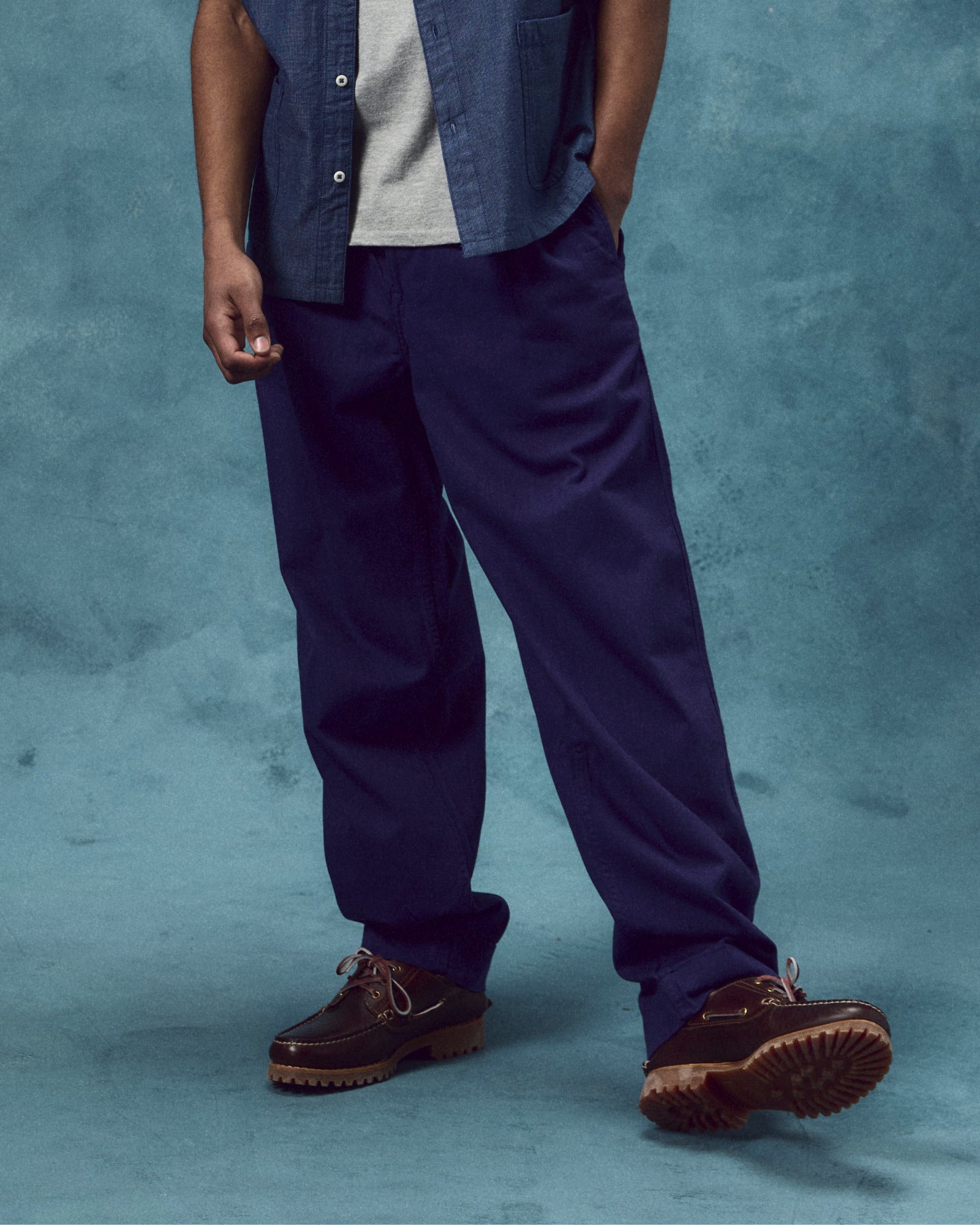 Side view of model wearing deep indigo 5022 barrel leg pants from Uskees. Showing baggy fit with taper at the hem, back pockets with flap and turn-ups.