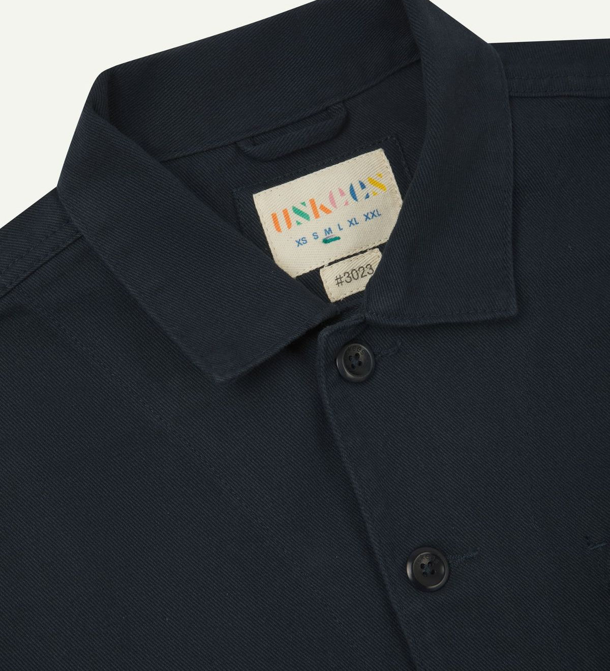 Front close view of blueberry-coloured organic cotton drill commuter blazer showing collar and  Uskees branding label.