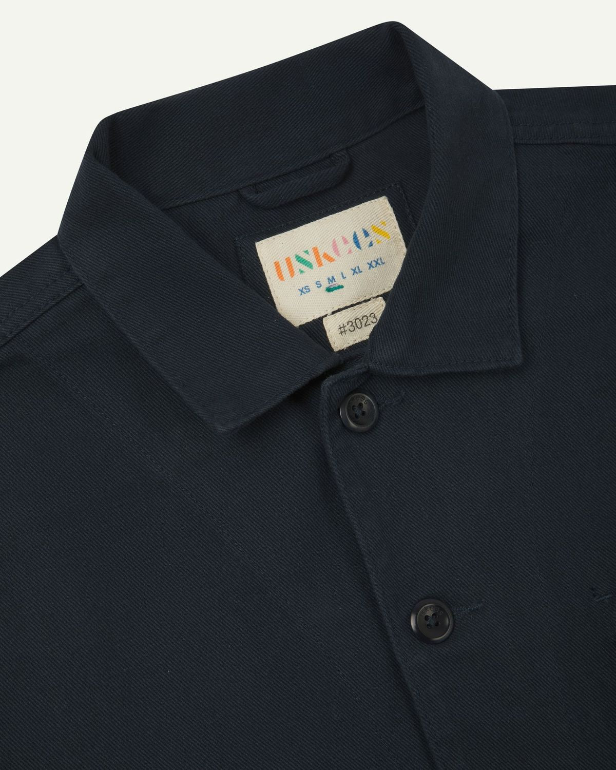 Front close view of blueberry-coloured organic cotton drill commuter blazer showing collar and  Uskees branding label.