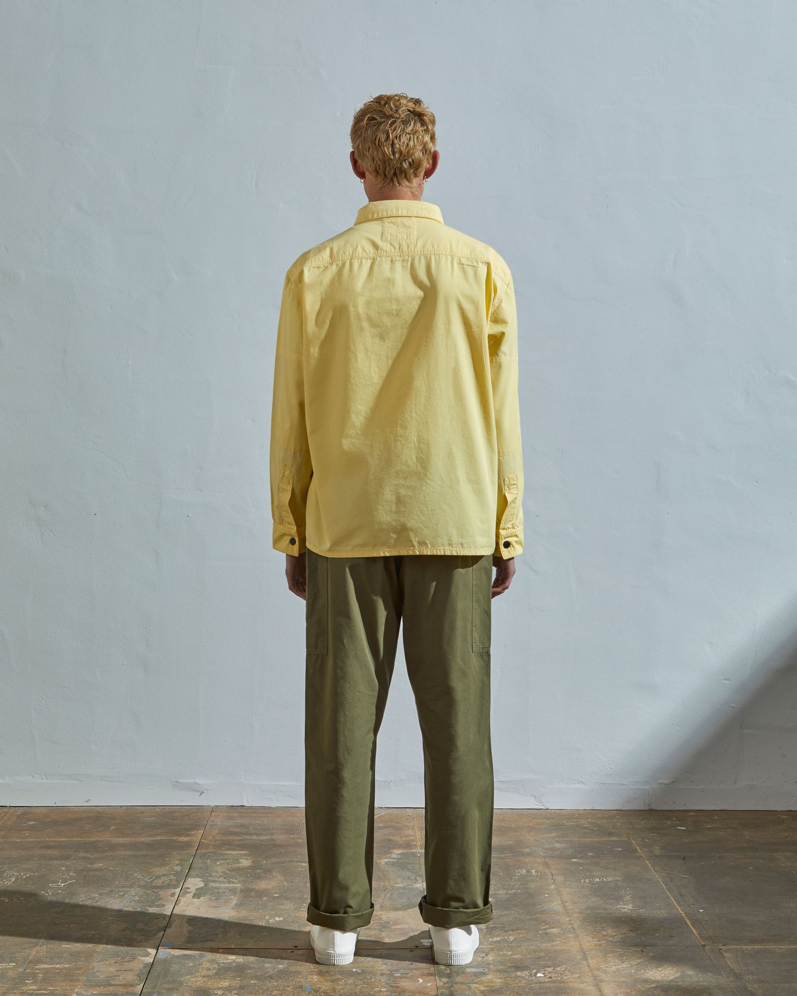 Full-length rear view of model wearing #6001, pale, banana-yellow over shirt showing reinforced elbows.