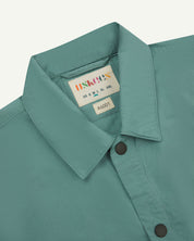 Front close-up view of the collar, popper buttons and Uskees branding label of the blue-green eucalyptus 6001 lightweight overshirt.