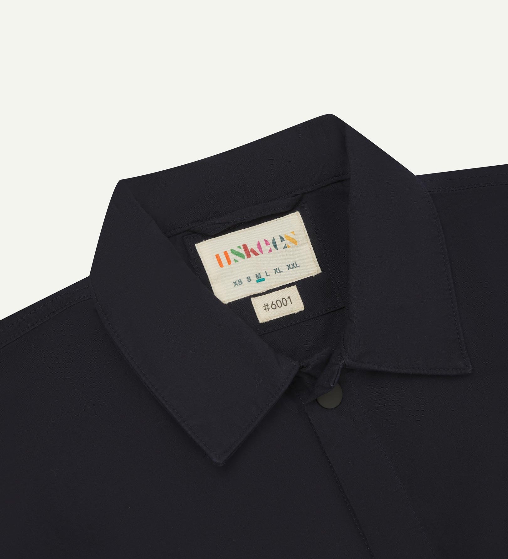 Front close-up view of the collar, popper buttons and Uskees branding label of the midnight blue 6001 lightweight overshirt.
