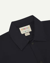 Front close-up view of the collar, popper buttons and Uskees branding label of the midnight blue 6001 lightweight overshirt.