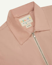 Front close-up view of the collar, zip detail and Uskees branding label of the dusty pink 6002 lightweight jacket.