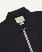 Front close-up view of the collar, zip detail and Uskees branding label of the midnight blue 6002 lightweight jacket.