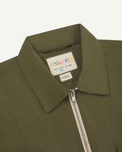 Front close-up view of the collar, zip detail and Uskees branding label of the olive-green 6002 lightweight jacket.