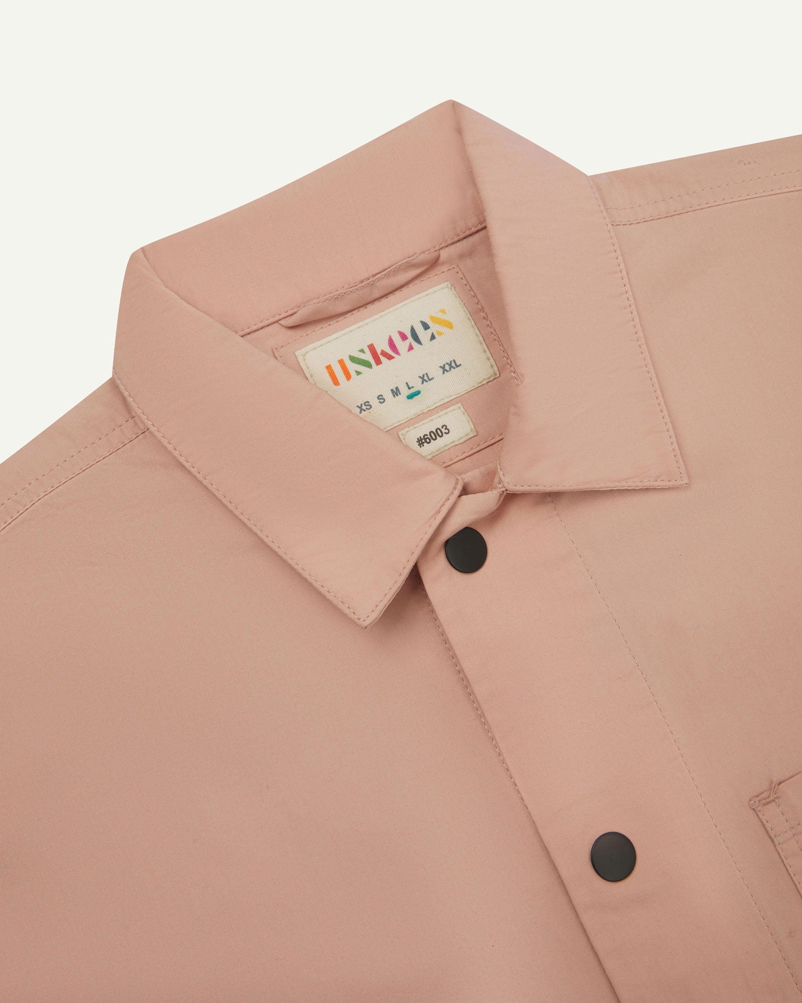 Close-up view of the #6003 reinforced shirt collar, showing weave of dusty pink organic cotton, contrast press studs and Uskees branding label.