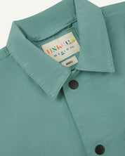 Close-up view of the #6003 reinforced shirt collar, showing weave of eucalyptus-green organic cotton, contrast press studs and Uskees branding label.
