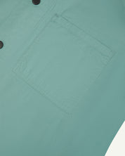 Angled mid-view of #6003 Uskees buttoned lightweight short sleeve shirt in eucalyptus-green with focus on breast pocket.