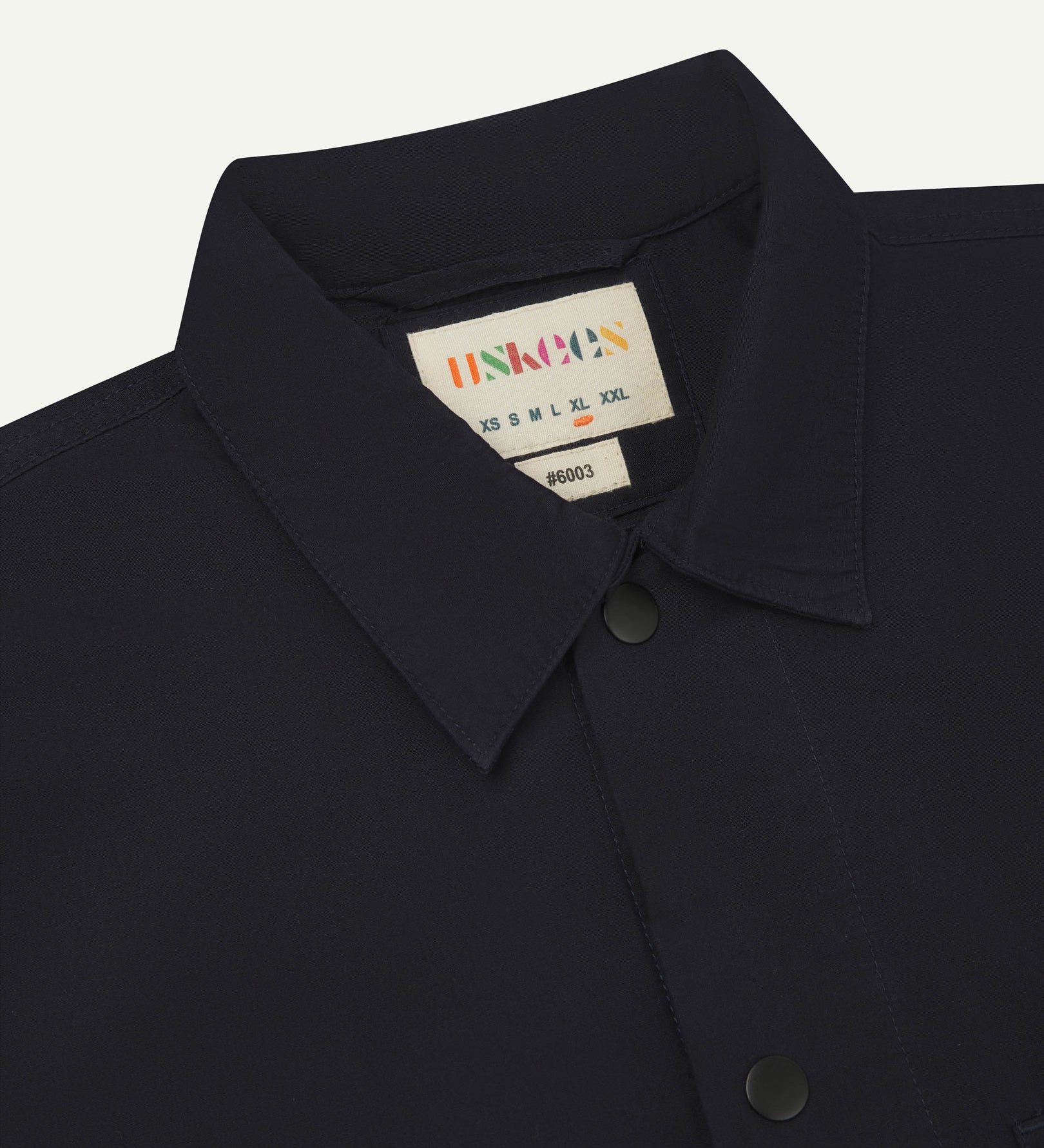 Close-up view of the #6003 reinforced shirt collar, showing weave of midnight blue organic cotton, contrast press studs and Uskees branding label.