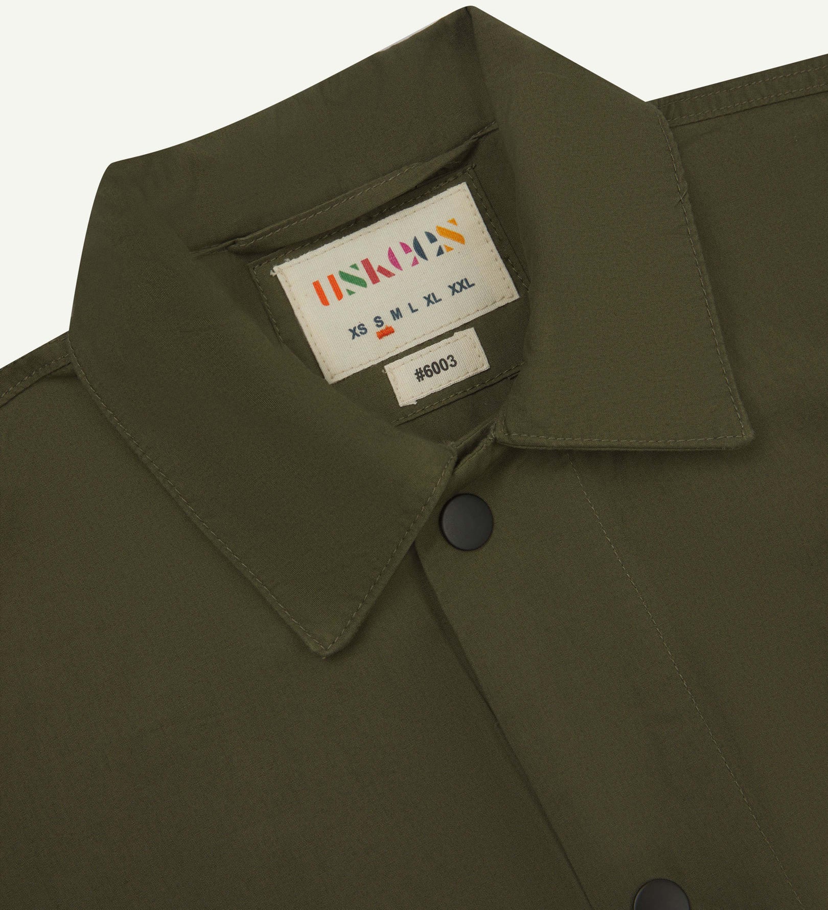 Close-up view of the #6003 reinforced shirt collar, showing weave of olive-green organic cotton, contrast press studs and Uskees branding label.