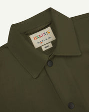 Close-up view of the #6003 reinforced shirt collar, showing weave of olive-green organic cotton, contrast press studs and Uskees branding label.