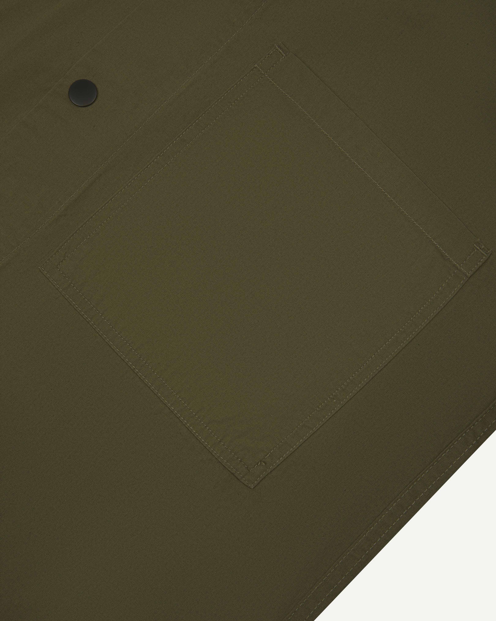 Angled mid-view of #6003 Uskees buttoned lightweight short sleeve shirt in olive-green with focus on breast pocket.