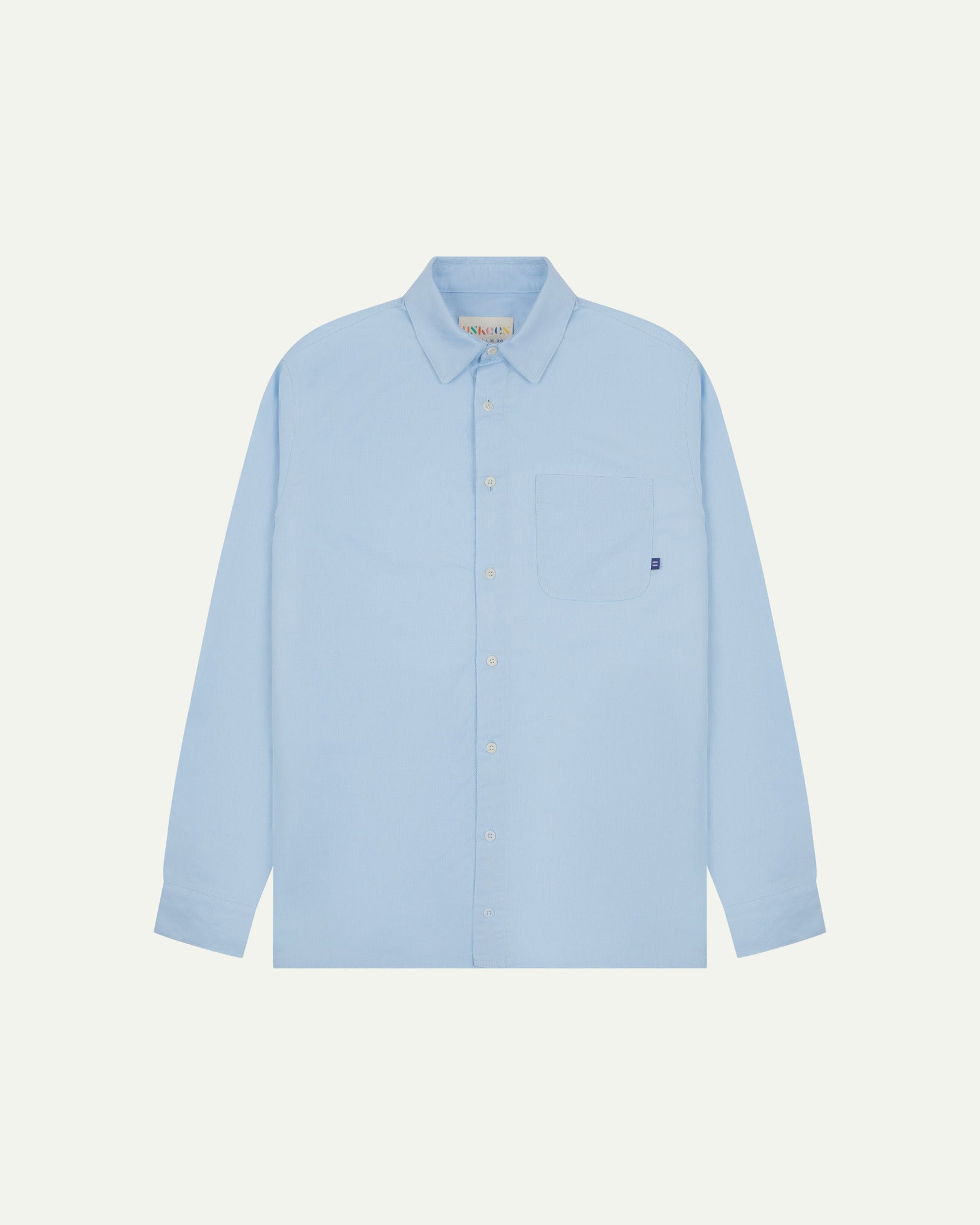 Flat front view of sky blue organic cotton Oxford shirt from Uskees. Clearly showing loose fit and 8-button front.