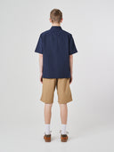Full-length back view of model wearing Uskees Tasker buttoned short sleeve shirt with dark blue fabric. Paired with khaki cargo shorts.