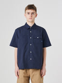 Top-half view of model wearing Uskees Tasker buttoned short sleeve shirt with dark blue fabric.