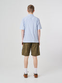 Full-length back view of model wearing Uskees Tasker buttoned short sleeve shirt with blue, gold and white striped cotton fabric. Paired with olive-green cargo shorts.