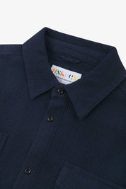 Close-up and angled front view of the 6007 Tasker shirt in deep blue, showing the waffle texture, collar, hanging loop and matching corozo buttons.