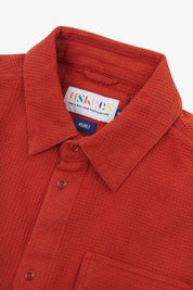 Close-up and angled front view of the 6007 Tasker shirt in rust-red, showing the waffle texture, collar, hanging loop and matching corozo buttons.