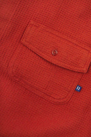 Angled mid-view of #6007 buttoned organic cotton waffle fabric short sleeve shirt in rust-red with focus on button down flap chest pocket and Uskees branding tag.