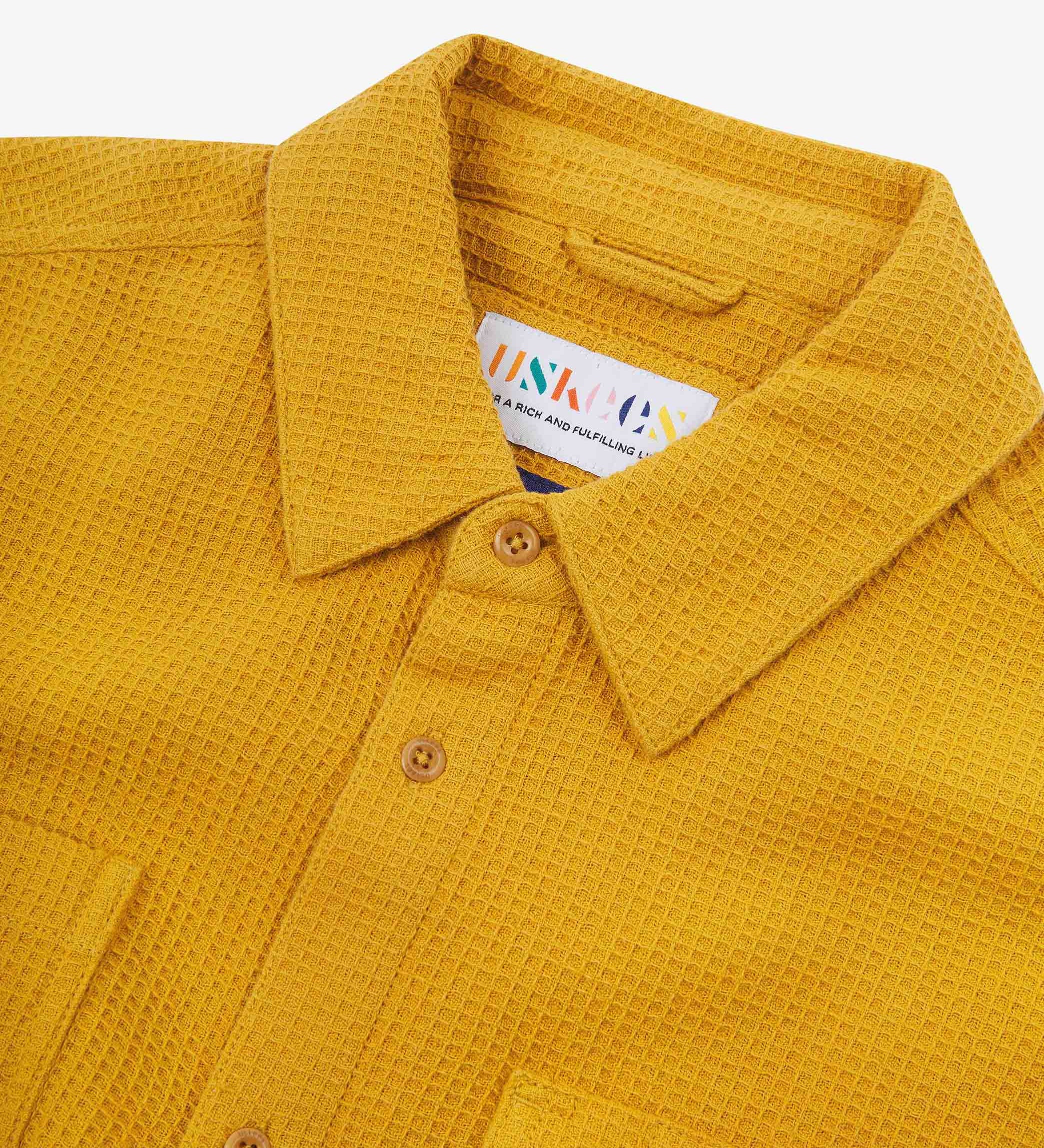 Close-up and angled front view of the 6007 Tasker shirt in yellow, showing the waffle texture, collar, hanging loop and matching corozo buttons.