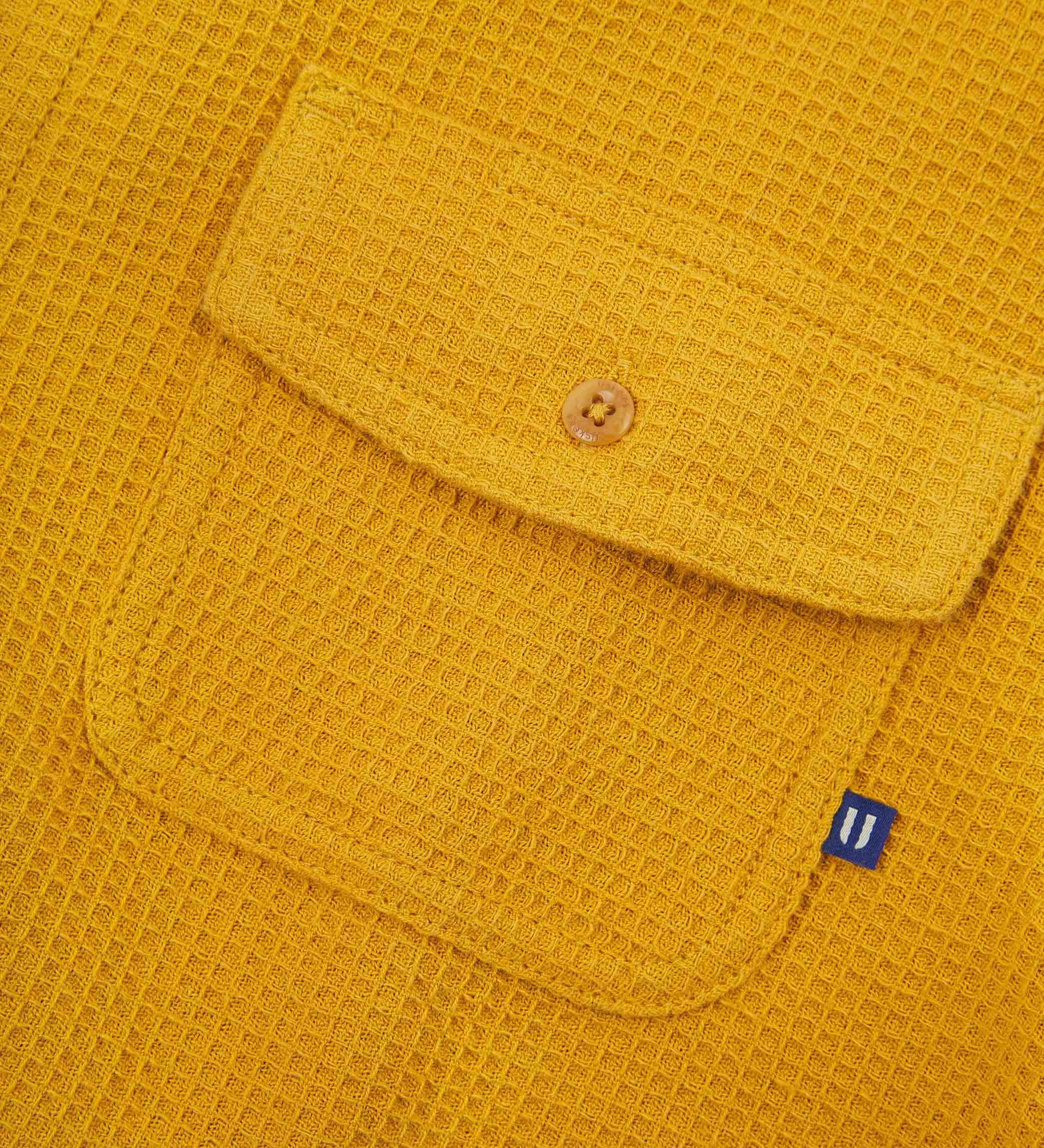 Angled mid-view of #6007 buttoned organic cotton waffle fabric short sleeve shirt in yellow with focus on button down flap chest pocket and Uskees branding tag.